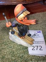 Side view of the vintage Hummel Skier Boy figurine standing on skis with poles, dressed in a red hat and scarf.