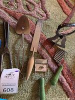 Top view of the vintage kitchen gadgets including pie server, tongs, spatula, crinkle cutter, and vegetable peeler alongside metal figurines on a carpet.