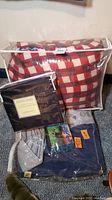 Clear photo of sleeping bag in transparent storage bag with red and white checkered pattern, queen sheets in unopened packaging, and blue twin air mattress with pump in plastic wrap.