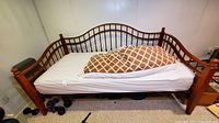 Full front view of the solid wood day bed with white mattress and diamond patterned throw pillow, showing curved spindle styling and rounded finials on posts.