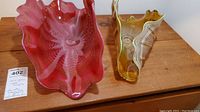 Two abstract ruffled glass sculptures side by side on wooden surface