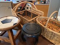 Overview of lot showing four wicker baskets of different styles and sizes, wooden soccer ball stool, and black Asian style plant stand grouped together.