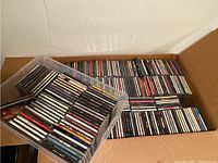CD collection arranged in a cardboard box and a clear plastic bin showing large quantity and mixed genres.