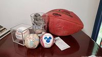 Wide view showing all items together on table, includes football, various baseballs, Patriots glass, and stones.