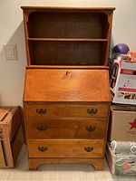 Front view of drop front secretary desk closed, showing three bottom drawers and open shelving compartment at top.