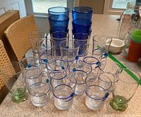 Full set of glasses including cobalt blue glasses, clear glasses with blue swirls, and clear glasses with green bases displayed on kitchen counter.