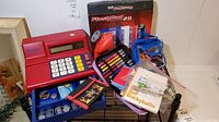 Toy cash register with keypad, display, play money in coin drawer, wallets, and FlashPad 2.0 in original box on shelving rack