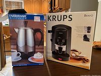 Krups Bravo cappuccino maker box standing next to Farberware Millennium percolator box in a kitchen setting.