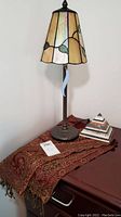 Full view of stained glass table lamp, layered stone pyramid paperweight, and Indian scarf wrap arranged on furniture.