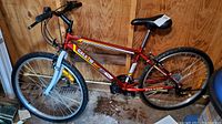 Side view of the red men's GalaXie Speed MTB mountain bike with 22" frame, front suspension fork, black saddle, and knobby tires indoors against wooden wall.