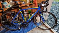 Full left-side view of blue/yellow Specialized road bike on shed floor