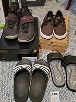 Four pairs of men's shoes on carpet floor: Nike sneakers on Adidas box, Sperry Topsiders on Sperry box, Adidas sandals, OP brand sliders.