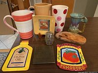 Overview photo with multiple pitchers, vases, trinkets including trivets, artisan dish, glass jar, wooden decor piece