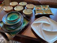 View of six cream pottery bowls, stacked green and brown glazed pottery pieces, and white divided plate with chip.