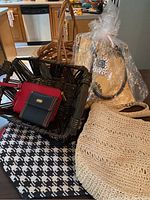 Photo shows two wicker baskets and multiple bags and purses arranged on a black and white houndstooth patterned surface in front of kitchen background.