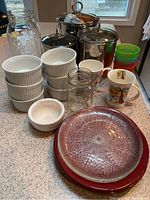 Mixed serving set including six white Dansk bowls stacked, an additional white ceramic bowl, two decorative china teacups, Mason jars without lids, colorful plastic cups and plates, and glass plates with some chips