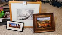 Three framed prints arranged on carpet: large black and white cityscape, medium sized Tuscan hills painting, and smaller Courthouse Towers photo.