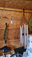 View of Woodstock Windsor Ger Chimes of Orpheus galvanized steel pipe wind chime hanging in a shed with six metal pipes suspended on black frame.