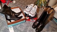 Three pairs of women's footwear displayed: black Peruzzi equestrian boots in a box, gray and white Avia sneakers on their box, black Life Style high heel boots standing.