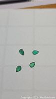 Four pear cut natural emerald gemstones laid out showing color and shape clearly.
