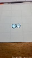 Two round sky blue topaz gemstones with glossy surfaces, showing color and clarity under light.
