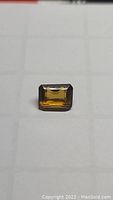 Top view of a rectangular emerald cut deep golden orange cognac citrine gemstone on a white grid background.