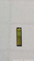 Light green rectangular baguette cut tourmaline gemstone viewed from above on a white background.