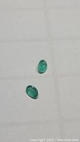 Two natural oval cut emeralds placed on a white background showing their size and color.