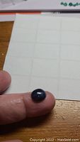 Blue oval cabochon star sapphire gemstone on fingertip highlighting size and shape.