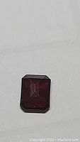 Front view of deep purple-red emerald cut rhodolite garnet gemstone on plain background