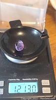 Pear shaped amethyst gemstone placed on digital scale showing weight of 12.13 carats.