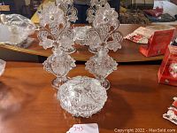 Set of two Irice crystal perfume bottles with stoppers and one powder jar placed on wooden surface in front of a mirror, showing clear intricate floral and grape designs.
