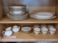 Shelf with stacked dinner plates and salad plates, rimmed soup bowls, teacups, saucers, creamer and sugar bowl.