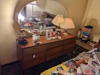 Full view of wooden dresser with nine drawers and attached oval mirror, top surface covered with decorative items
