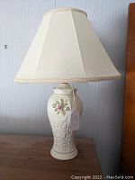 Full view of the Belleek porcelain lamp with cream fabric shade on wooden surface, showing shape and overall look.