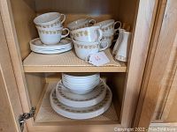 Photo showing cups stacked on saucers and salt and pepper shakers on a shelf
