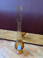 Full view of amber colored tall glass vase with a scalloped top and pedestal base.