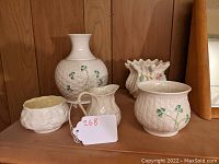 Front view of five Belleek porcelain pieces on wooden shelf showing shamrocks and gold accents.
