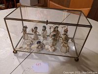 Full view of the glass and brass display case housing Nativity figurines including Mary, Joseph, Wise Men, angels, baby Jesus laying down, and lambs, placed on a wooden surface.