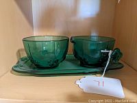 Photo showing green glass creamer, sugar bowl, and tray set placed on a shelf.