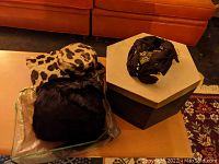 Photo showing group of two women's hats and two muffs; leopard print and black fur muffs, dark fabric hat with bow next to hexagonal hat box