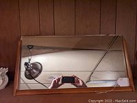 Front view of the rectangular mirror with warm wood frame leaning against a wall, showing the reflective surface and rounded wooden edges.