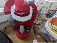 Front angle of red Keurig coffee maker with a reusable coffee pod in place and chrome wire pod holder in background