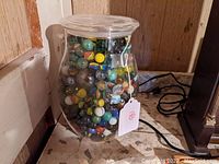 Front view of a clear glass jar filled with colorful glass marbles