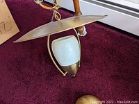 Brass hanging light fixture showing the frosted glass shade under a large brass shade, hanging chain and electrical cord visible.