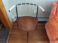 Front view of the mid-century chair showing triangular plywood seat with smooth wood patina, tubular steel frame, and white/black vinyl woven backrest