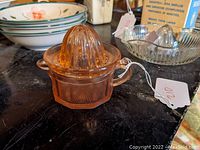 Pink Depression Glass Straining Juice Reamer with Under Cup shown from a side angle on black surface with price tag attached.
