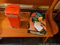 Red London phone booth-shaped candy tin and Pocket Simon game in original box on wooden bench.
