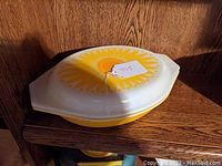 Photo of the oval divided dish with daisy-patterned lid sitting on a wooden shelf.