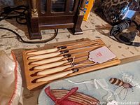 Set of six steak knives with ivory-colored handles laid out on a wooden knife holder.
